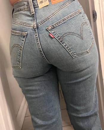 Person wearing fitted light-wash jeans in a fitting room, showcasing the back pockets and brand tag