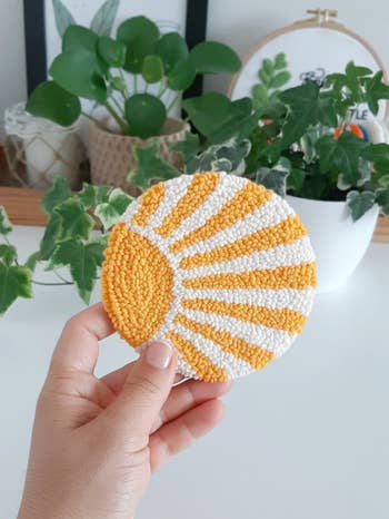person holding up the punch needle coaster with yellow sun on it