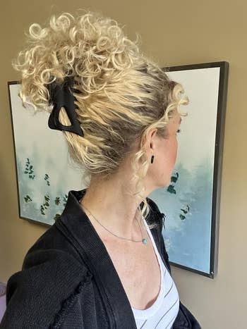 Reviewer with curly hairsbreadth styled successful a hairsbreadth clip, wearing a achromatic overgarment implicit a striped top, stands successful beforehand of a painting