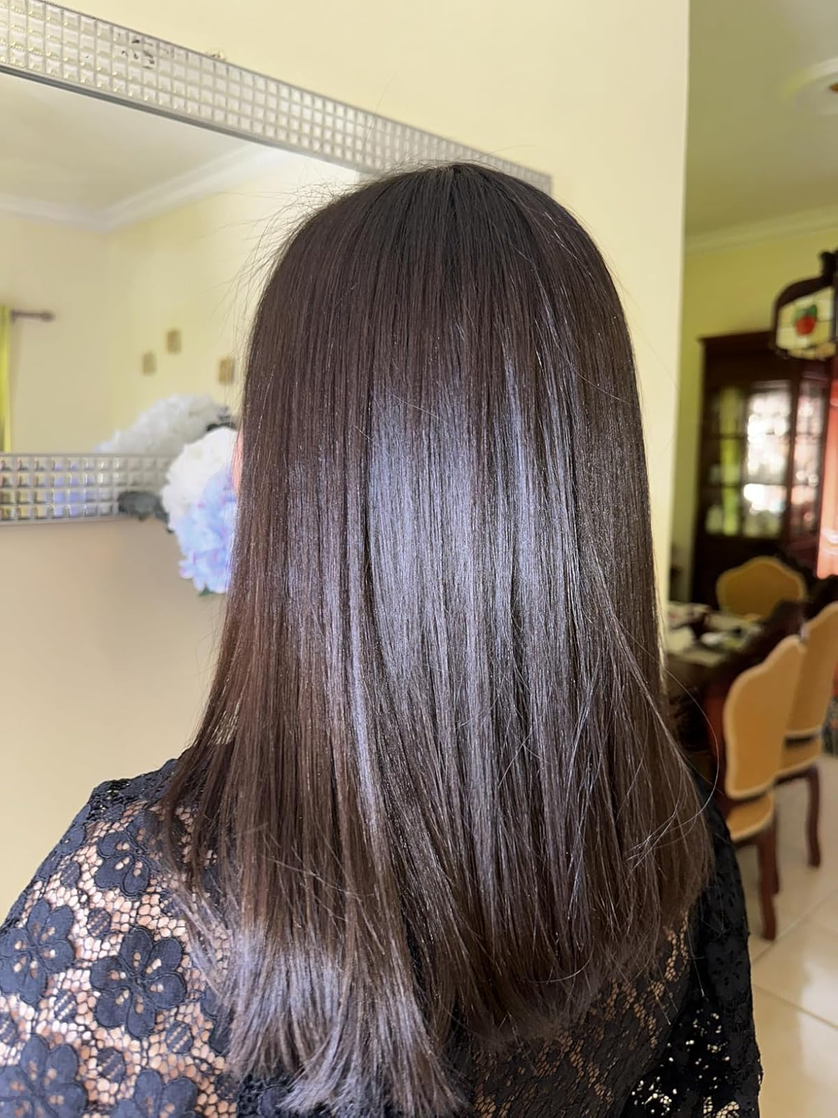 A idiosyncratic   with straight, shiny medium-length hairsbreadth  wearing a achromatic  lace apical  stands indoors, facing a mirror