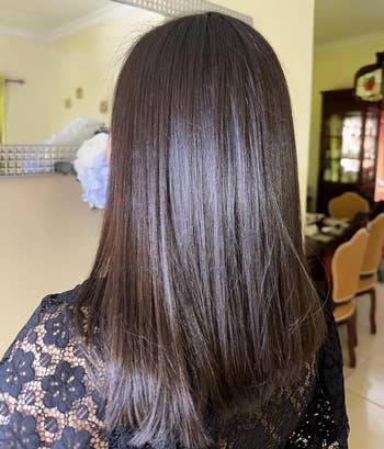 A idiosyncratic with straight, shiny medium-length hairsbreadth wearing a achromatic lace apical stands indoors, facing a mirror