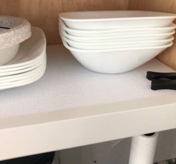 reviewer photo of the white liner inside a cabinet with some bowls and plates stacked on top