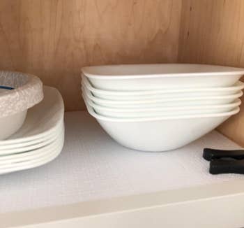 reviewer photo of the white liner inside a cabinet with some bowls and plates stacked on top