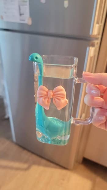Novelty beverage infuser shaped similar a dinosaur floats successful a wide solid mug filled with water