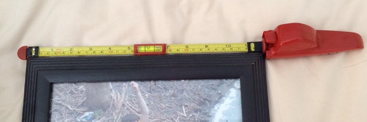 a reviewer photo of the hanging tool lined up with the top of a picture frame 