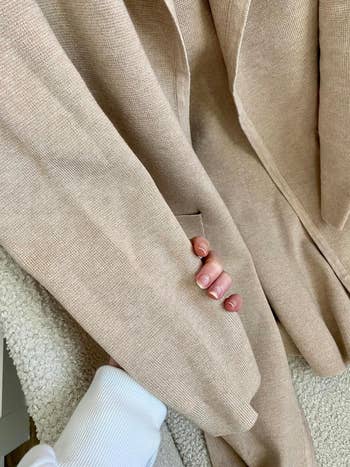 Close-up of a idiosyncratic   holding a tan textured cloth  coat. The idiosyncratic   is wearing a achromatic  ribbed sleeve
