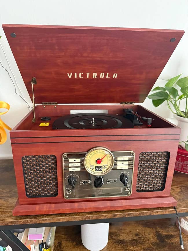 Vintage-style Victrola grounds   subordinate    connected  woody  stand, surrounded by plants and books