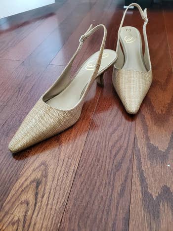 Stylish brace of pointed toed slingback heels with a woven texture, displayed connected a woody floor. Ideal for a chic and modern wardrobe update