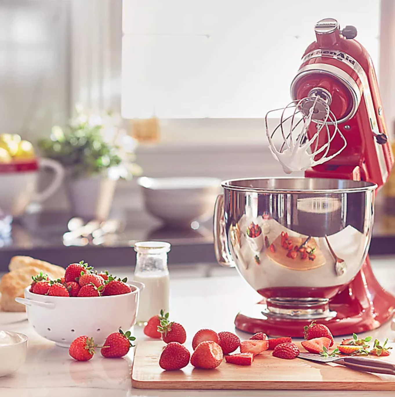 a red kitchenaid stand mixer with strawberries around it