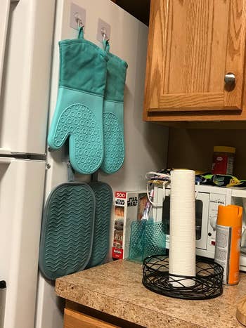 a reviewer's two teal oven mitts hanging on the side of their fridge
