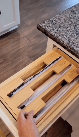 person using the organizer in a drawer to cut a piece of plastic wrap