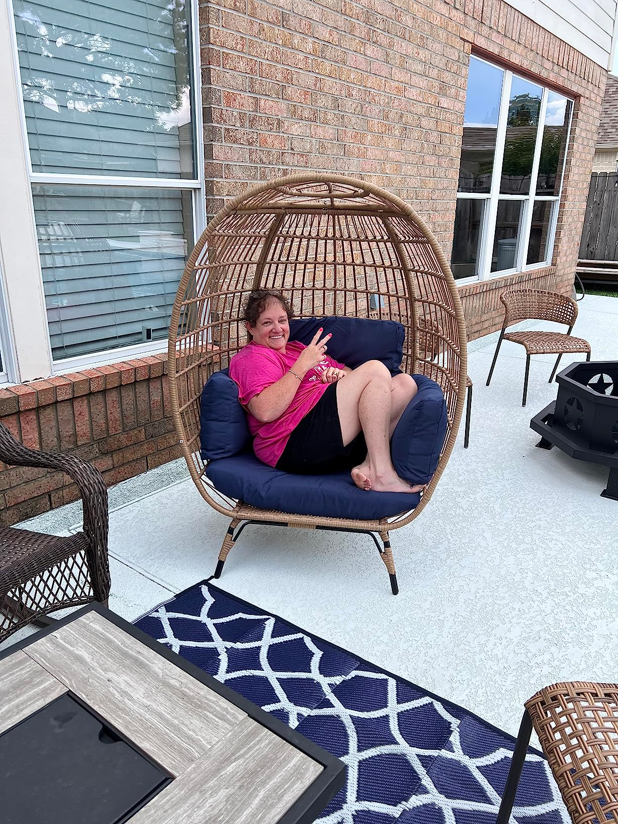 Person sitting successful  a wicker ovum  seat  connected  a patio, giving a bid    sign. The setup includes different   wicker furnishings  and a patterned outdoor rug