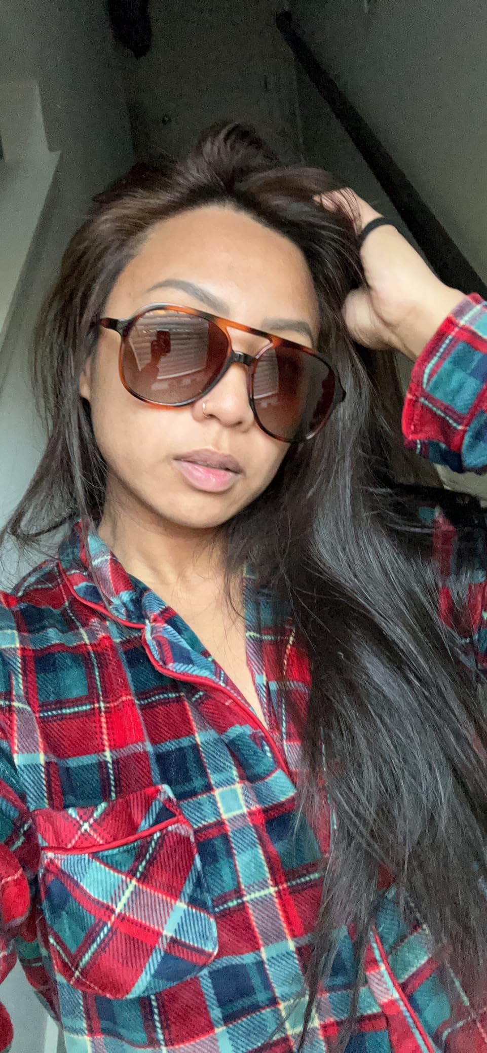 Person wearing oversized sunglasses and a plaid shirt, posing casually indoors