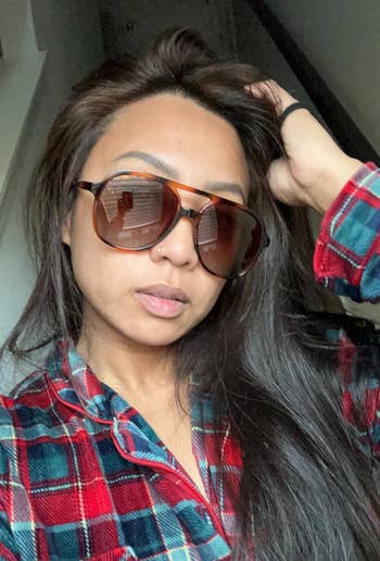 Person wearing oversized sunglasses and a plaid shirt, posing casually indoors