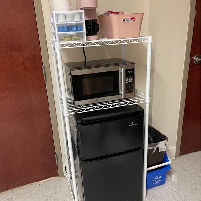 Microwave on shelving unit above a mini fridge