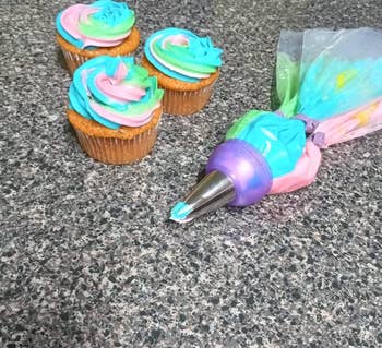 three piping bags attached with one coupler and tip and cupcakes it was used to decorate with pink blue and green frosting