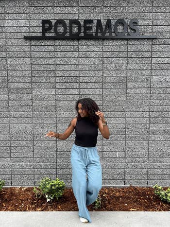 Person successful  achromatic  sleeveless apical  and wide-legged pants poses successful  beforehand   of a partition  with 