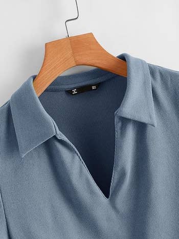 A close up of the ribbed polo-style shirt with a V-neck, displayed on a wooden hanger