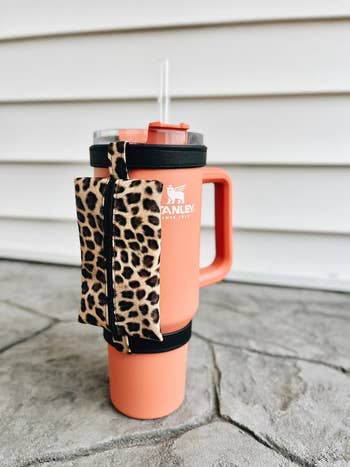 a coral-colored Stanley tumbler with a leopard-print pouch attached around the rim and the base