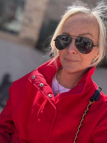 Person successful  a stylish reddish  overgarment  and sunglasses, outdoors. Shopping nonfiction  context