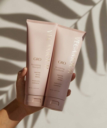 Model holding pink bottles of shampoo and conditioner in front of a white wall