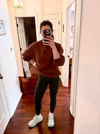 Person successful  casual outfit with a brownish  sweatshirt, leggings, and sneakers takes a selfie successful  a mirror, highlighting comfortable, mundane  fashion