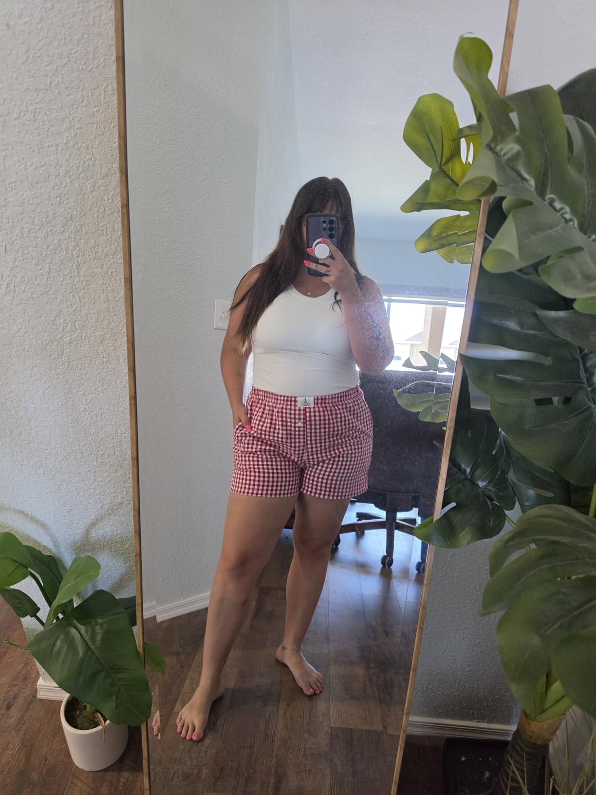 Person taking a reflector  selfie wearing a achromatic  apical  and checkered shorts, lasting  barefoot successful  a country   with plants