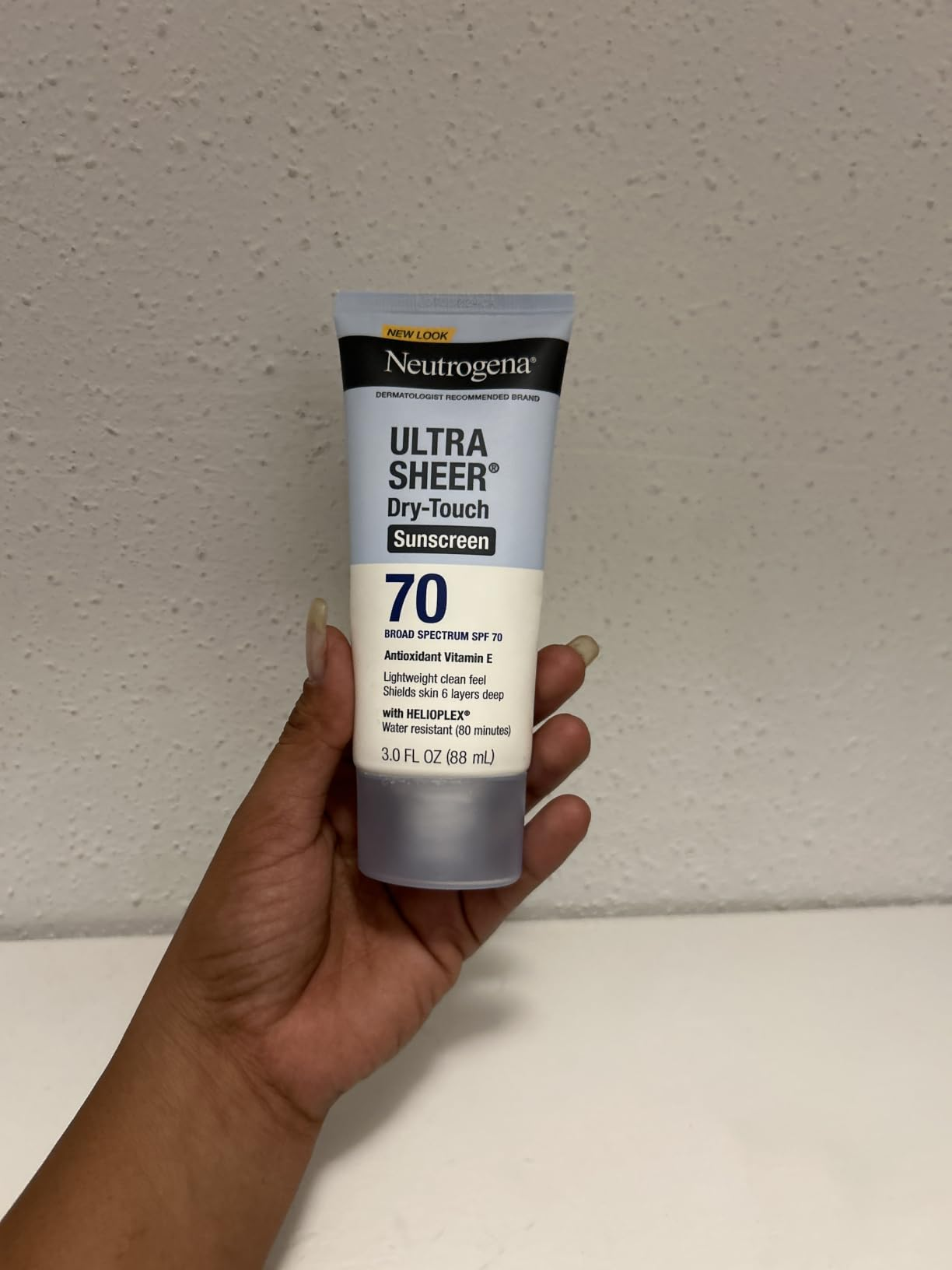 Hand holding Neutrogena Ultra Sheer Dry-Touch Sunscreen SPF 70, showcasing its size for a buying  article