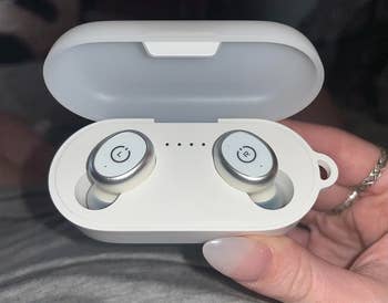 reviewer holding up the white earbuds in their matching case