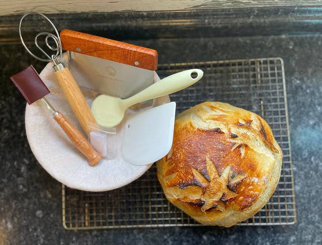 Artisan breadstuff with flour designs beside a handbasket of baking tools connected a cooling rack