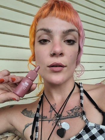 reviewer holds pink bottle of the Velvet Lip Tint while wearing it on lips