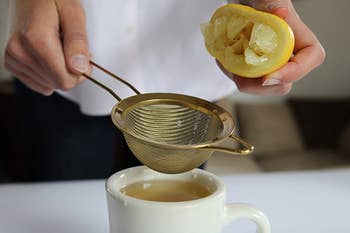 hand holding the gold small colander, using it to add lemon juice to tea