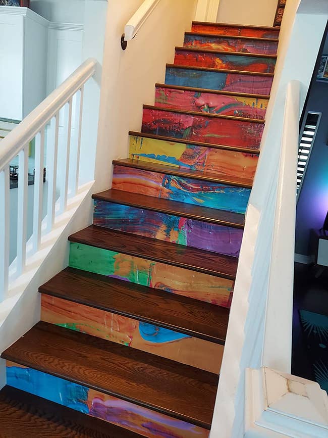 A set of stairs decorated with rainbow paint decals under each step 