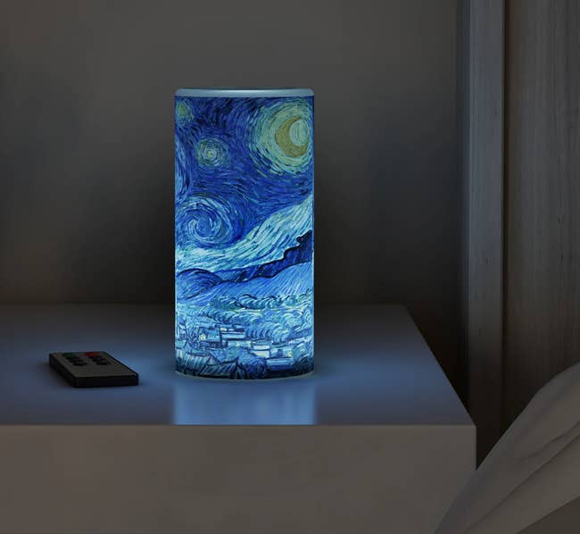 Flameless candle with depiction of a the painting Starry Night sitting atop a side table next to remote