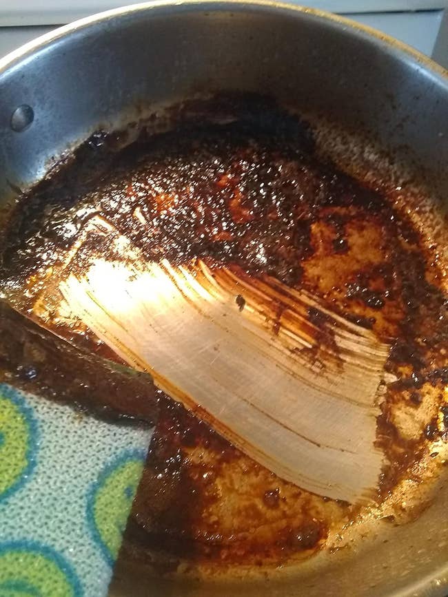 A burned pan with residue with a clean wipe in the middle showing how powerwash cut through the baked-on grease