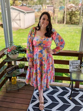 reviewer in a flowy floral dress with sheer sleeves, standing on a porch. Perfect spring attire for a sunny day out