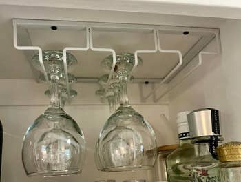 Wine glasses bent  upside down   from a mounted rack successful  a cabinet, with assorted  bottles disposable   nearby, showcasing a neat room  enactment     solution
