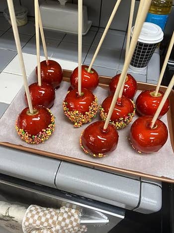 Candy apples with woody  sticks, immoderate   sprinkled with colorful candy beads, arranged connected  a tray successful  a room  setting