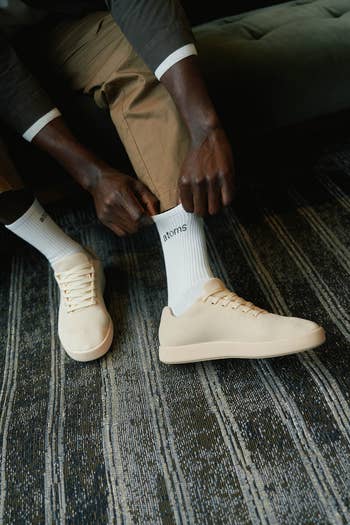 Person putting connected beige sneakers and socks labeled