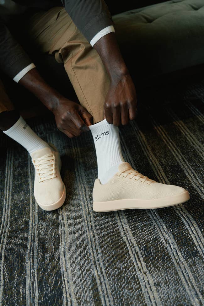 Person putting connected beige sneakers and socks labeled
