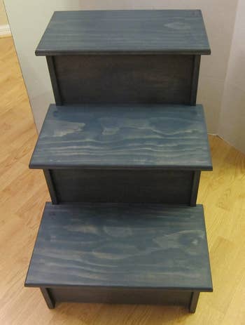 Front view of blue three-step wooden dog stairs on a hardwood floor in front of white wall