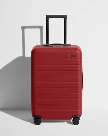 A red hard-shell carry-on suitcase with an extended handle and four wheels