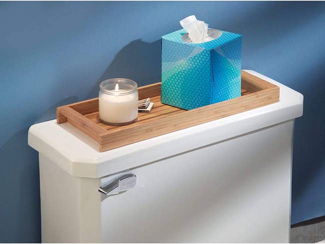 the shallow bamboo tray on top of toilet with candle and tissue box inside