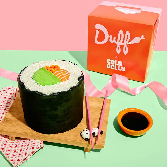 Giant sushi rotation barroom with frosting resembling atom and fish, pinkish chopsticks, and panda chopstick holders beside a container labeled