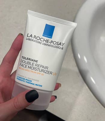 Person holding La Roche-Posay Toleriane Double Repair Face Moisturizer with SPF 30 adjacent a sink
