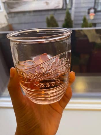 A hand holds a clear mason jar with the word