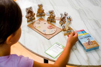 Child playing with a Cat Crimes board game, placing animal figures on a game board