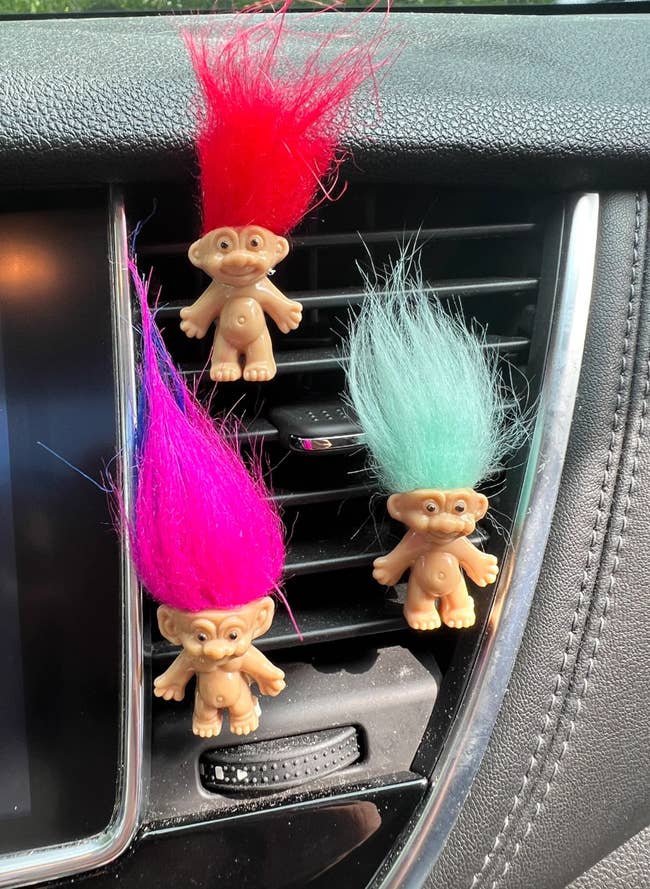 Three troll dolls with colorful hairsbreadth (red, pink, and airy blue) bent from a car's aerial vent