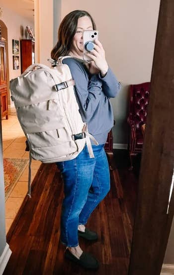 reviewer in a casual outfit takes a selfie with a large backpack, reflecting a practical yet stylish choice for shoppers