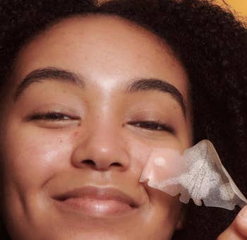 person smiling while applying a skincare patch to her face. Text reads: